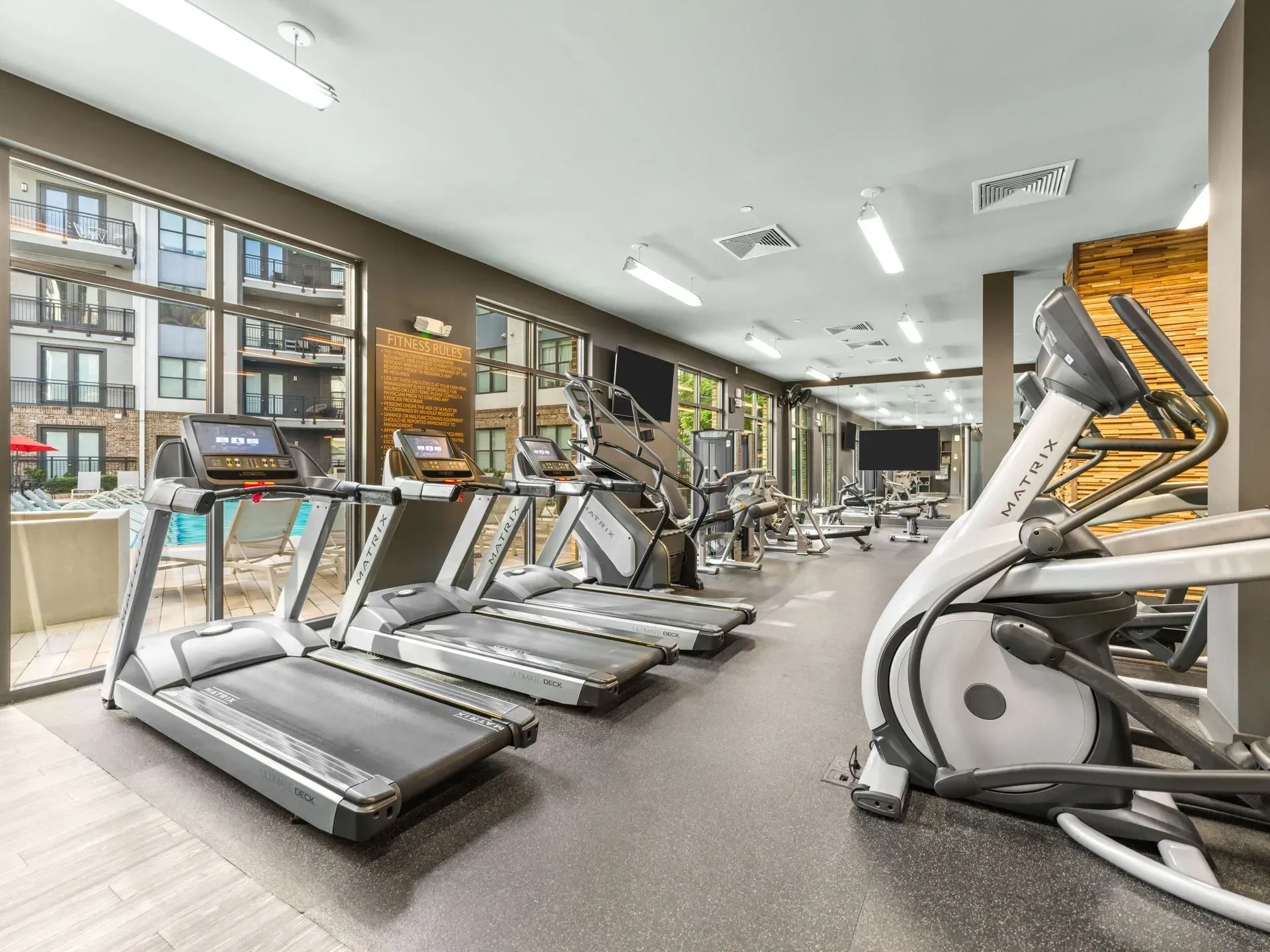 Bright gym with treadmills, cardio machines, and large windows overlooking city buildings