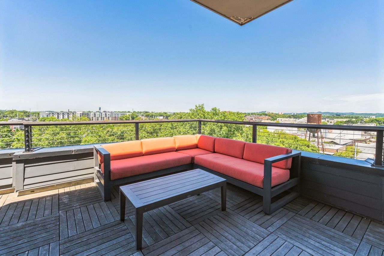 Rooftop terrace with an orange-cushioned sectional sofa and a coffee table, overlooking a cityscape.