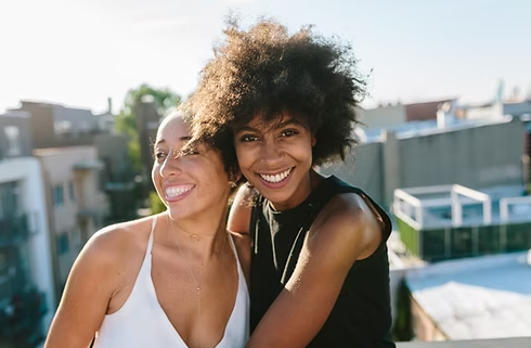 Two women are hugging each other on a rooftop and smiling for the camera.