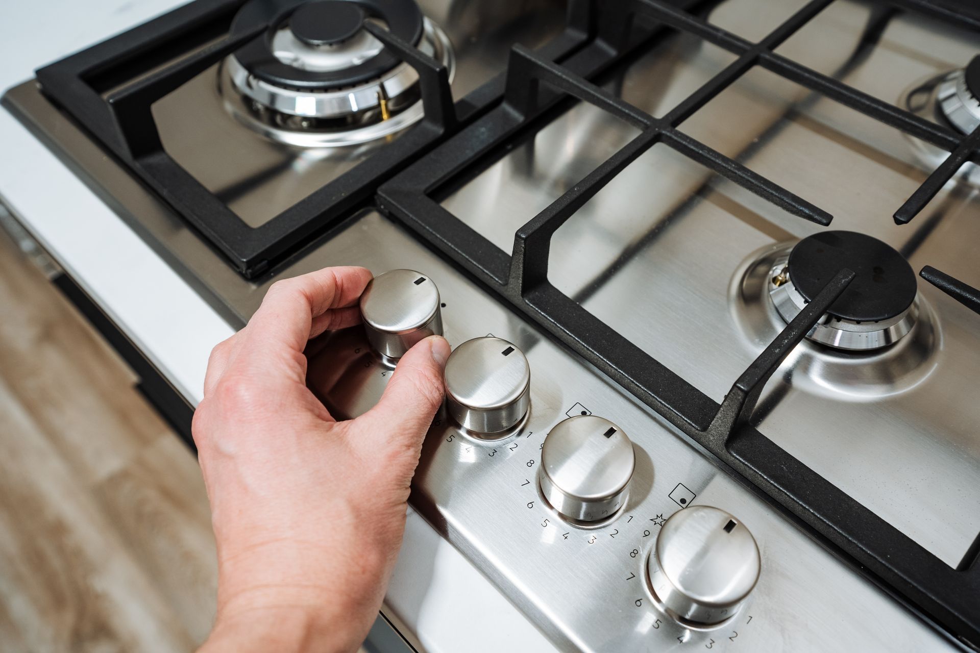 Close-up of modern range stove control knobs during appliance inspection. Hand adjusting control knob on a stainless steel gas cooktop.