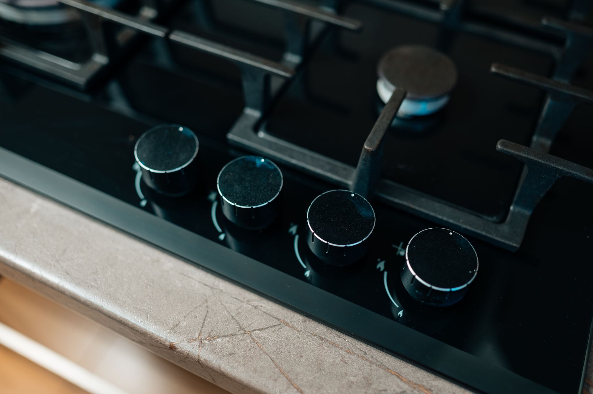 Black gas cooktop with control knobs and a lit burner on a kitchen counter.