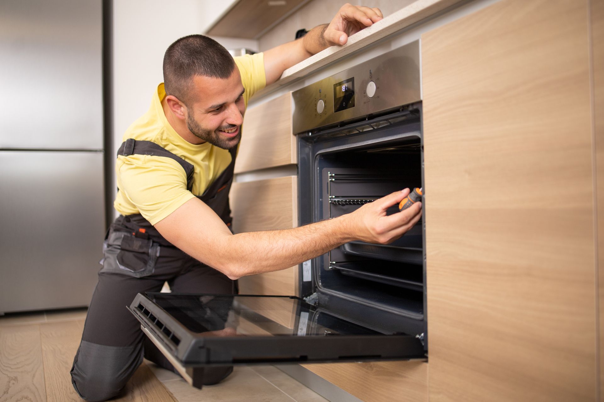 A man is fixing an oven in a kitchen, demonstrating his range repair skills using various tools.
