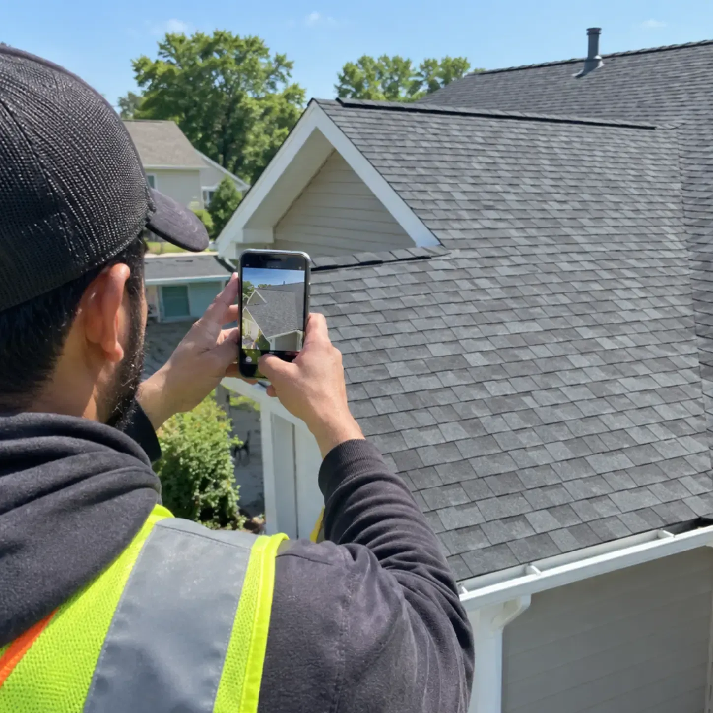 Roofing crew member photographing a finished asphalt shingle roof replacement with a phone Roofing crew member photographing a finished asphalt shingle roof replacement with a phone