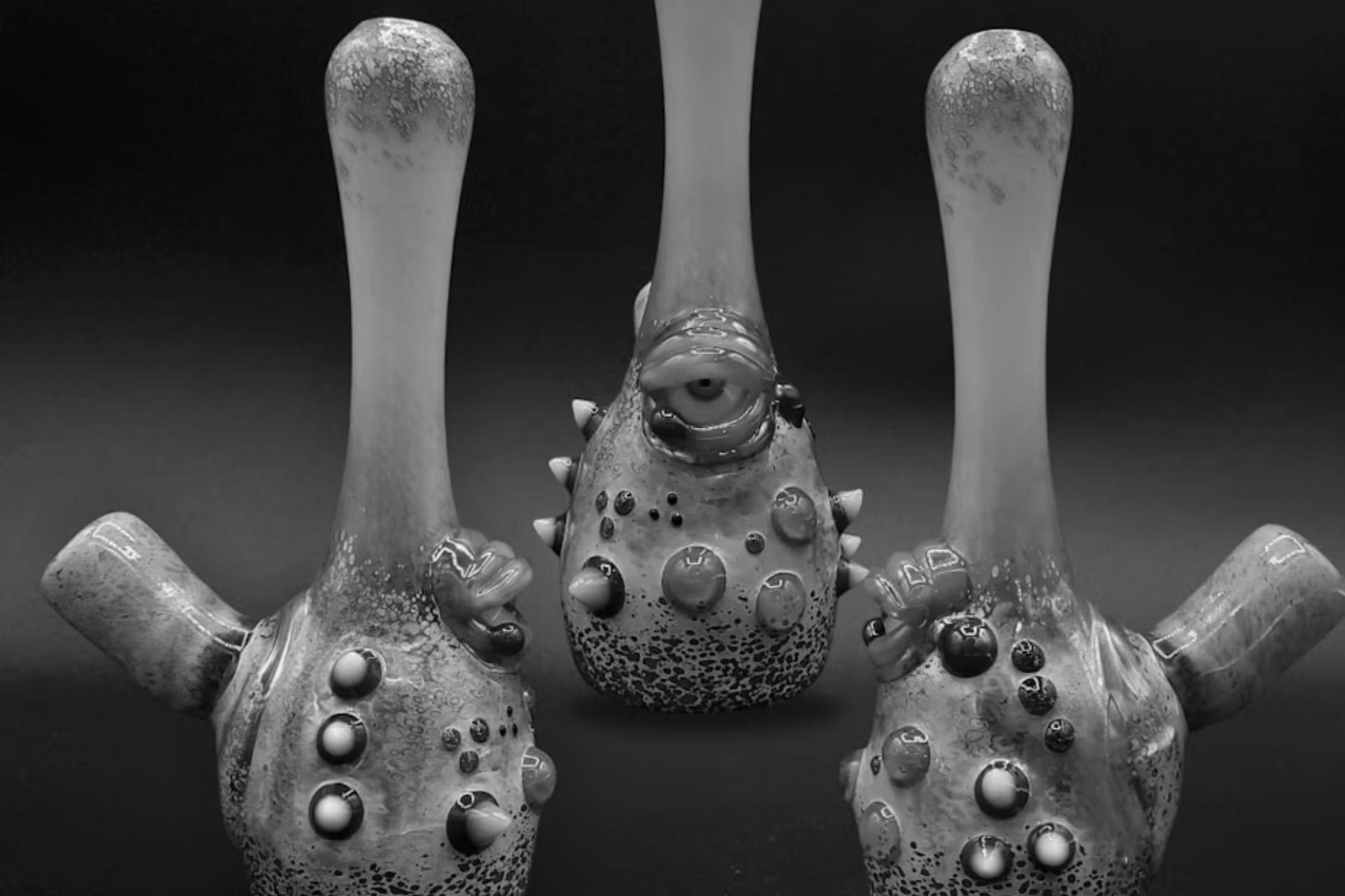 Three unique, handmade glass pipes with textured, speckled patterns and bulbous decorations arranged against a dark background.