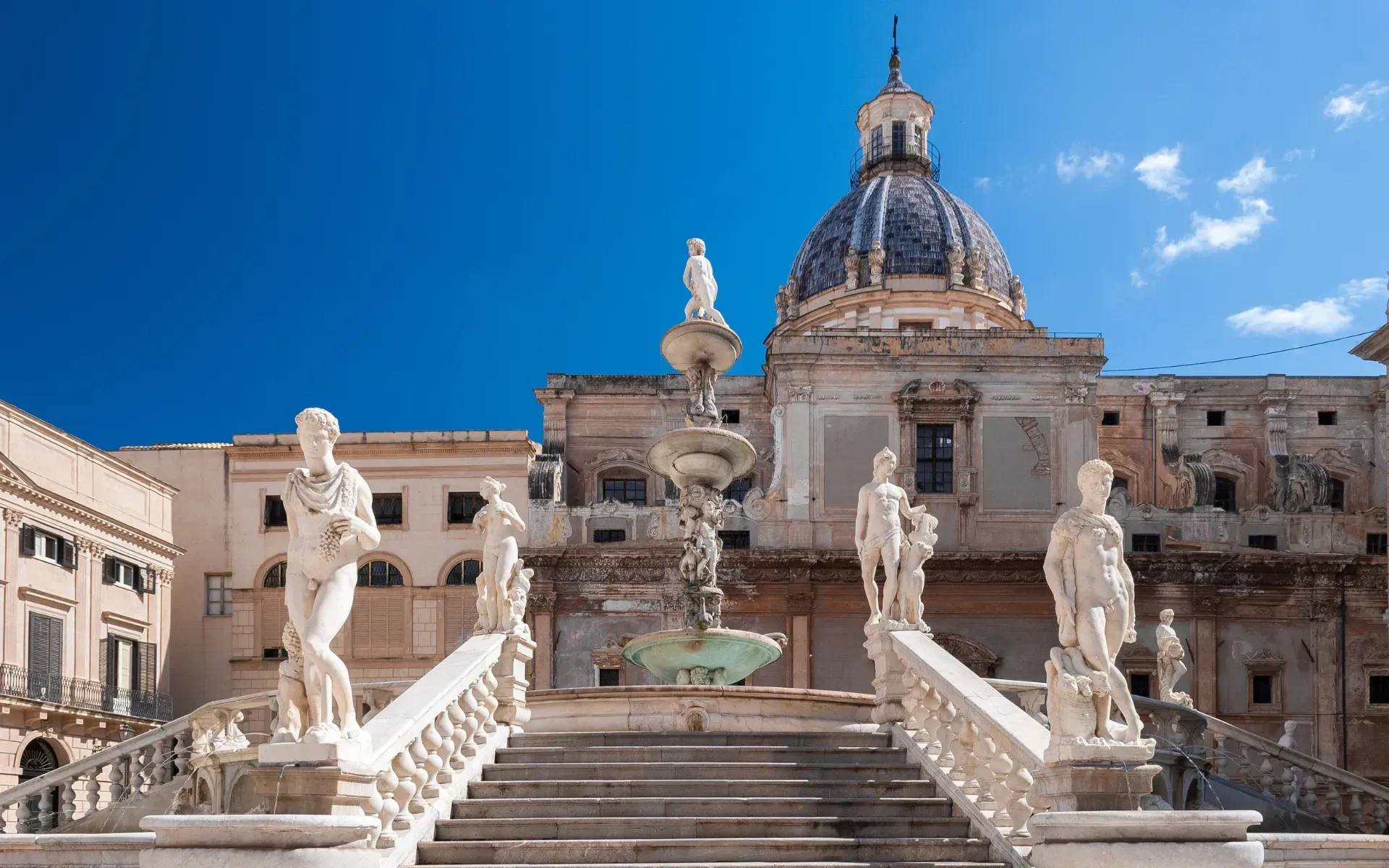 Fontaine et statues devant un bâtiment à dôme, sous un ciel d'un bleu éclatant à Palerme, en Italie.