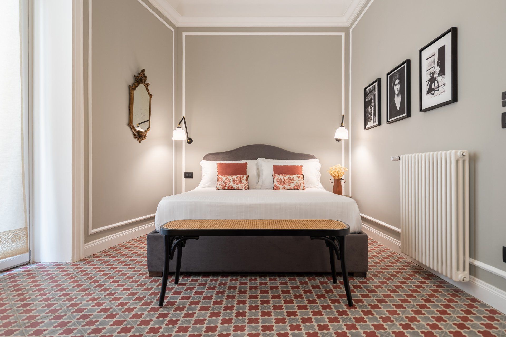Chambre avec lit, banc et œuvres d'art ; murs gris, sol carrelé rouge et blanc.