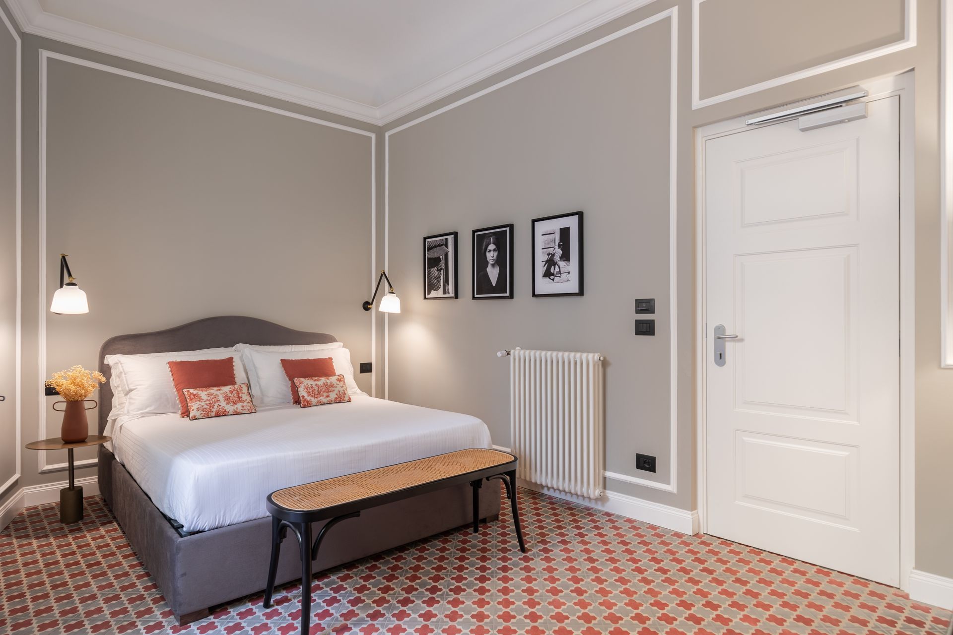 Chambre avec lit, banc, table de chevet, décoration murale, radiateur et porte blanche.