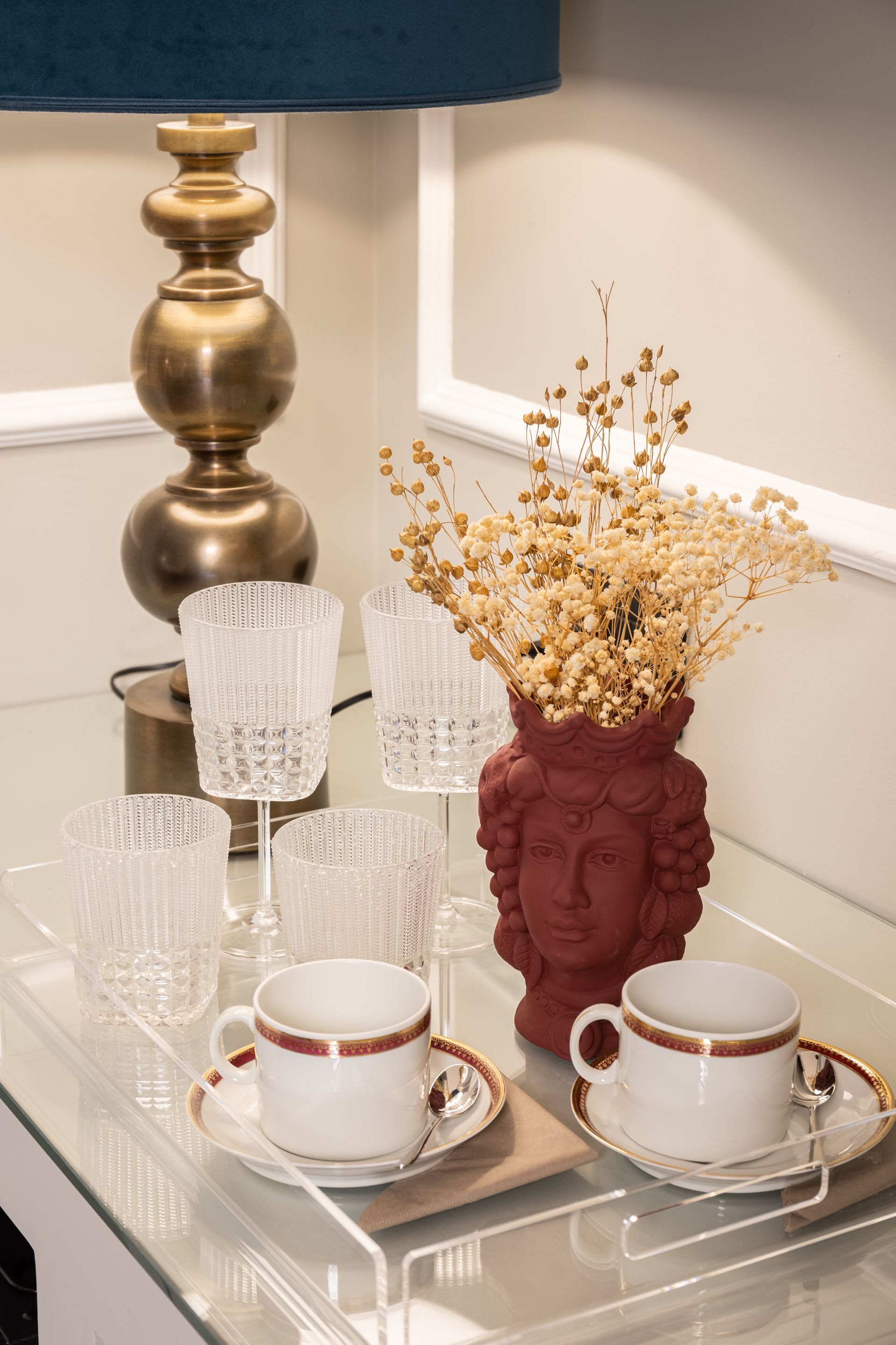 Tavolo con lampada, bicchieri, tazze da tè e vaso con fiori secchi.