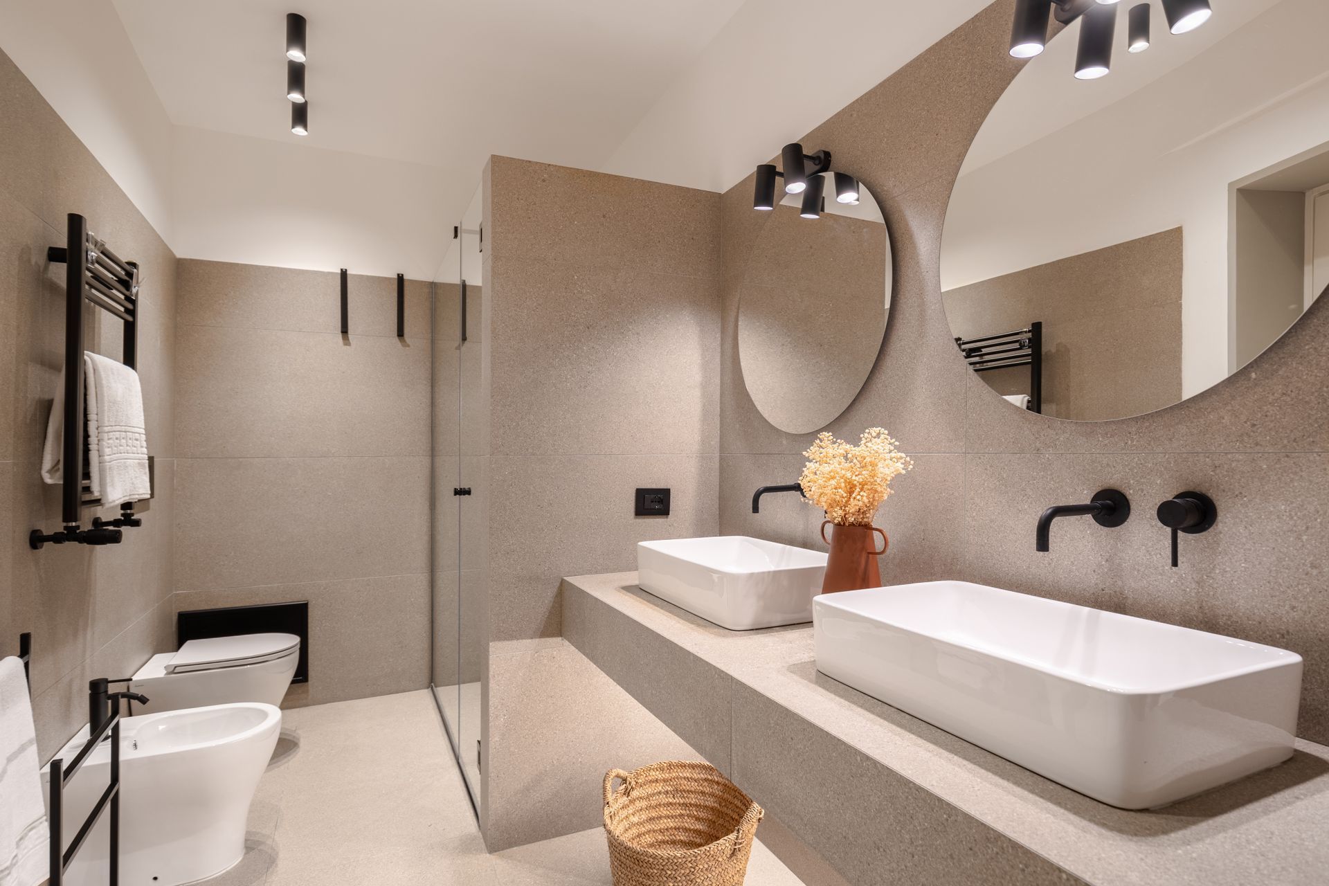 Bagno moderno con due lavandini, due specchi rotondi e pareti dai colori neutri.