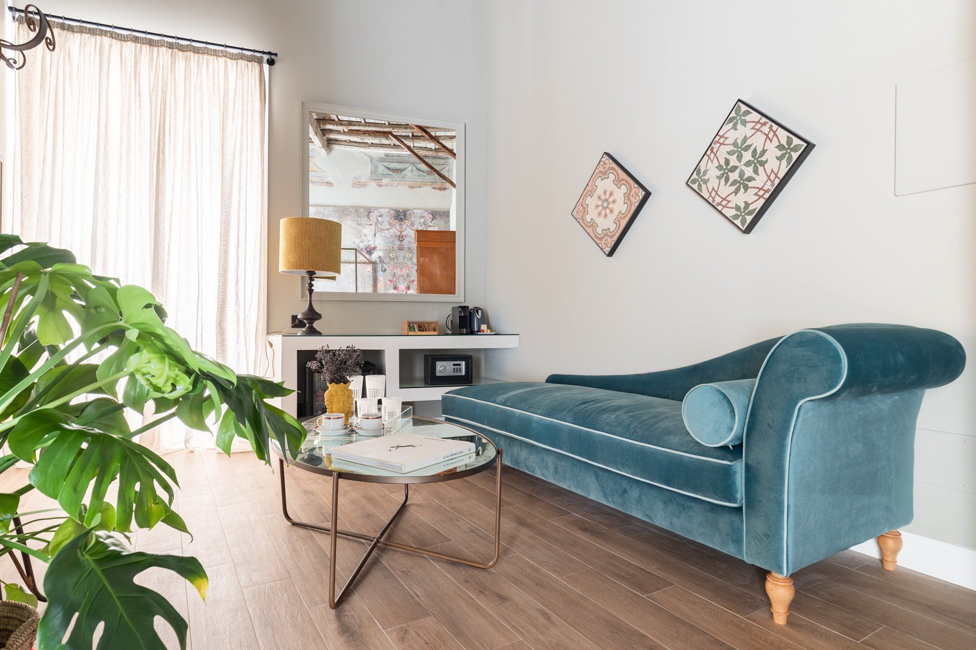 Soggiorno con chaise longue verde acqua, tavolino, pianta di monstera, piastrelle decorative e una finestra.
