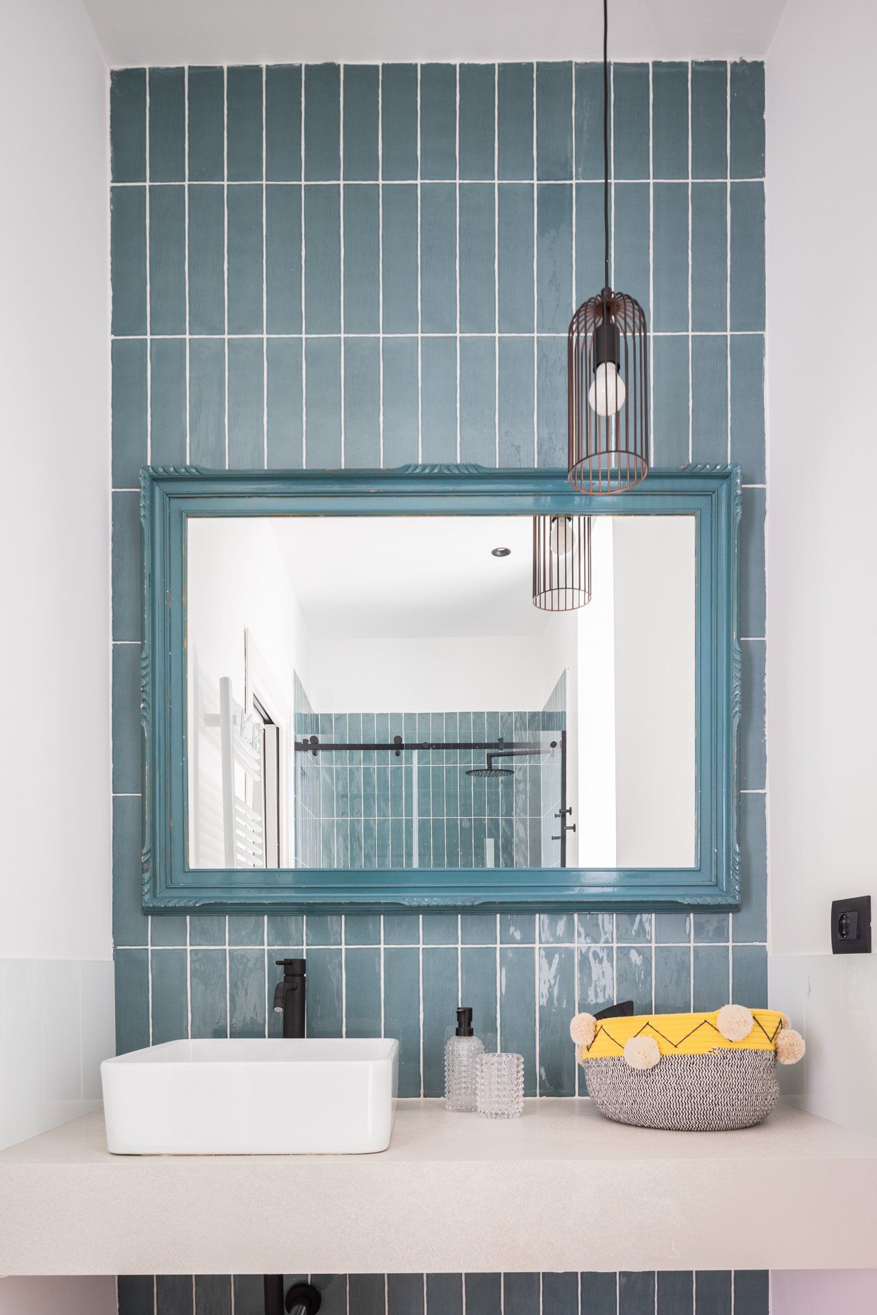 Bagno con piastrelle color verde acqua, specchio, lavandino rettangolare e lampada a sospensione.