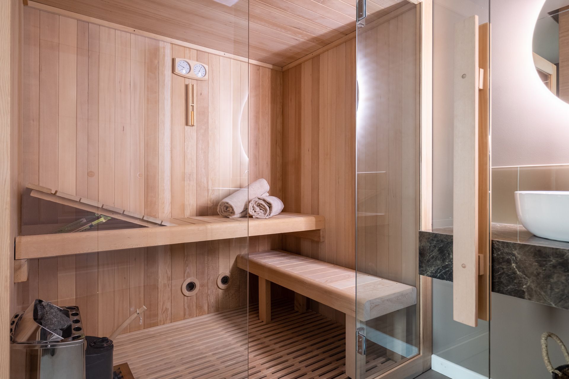 Small wooden sauna with glass door, bench, and towels.