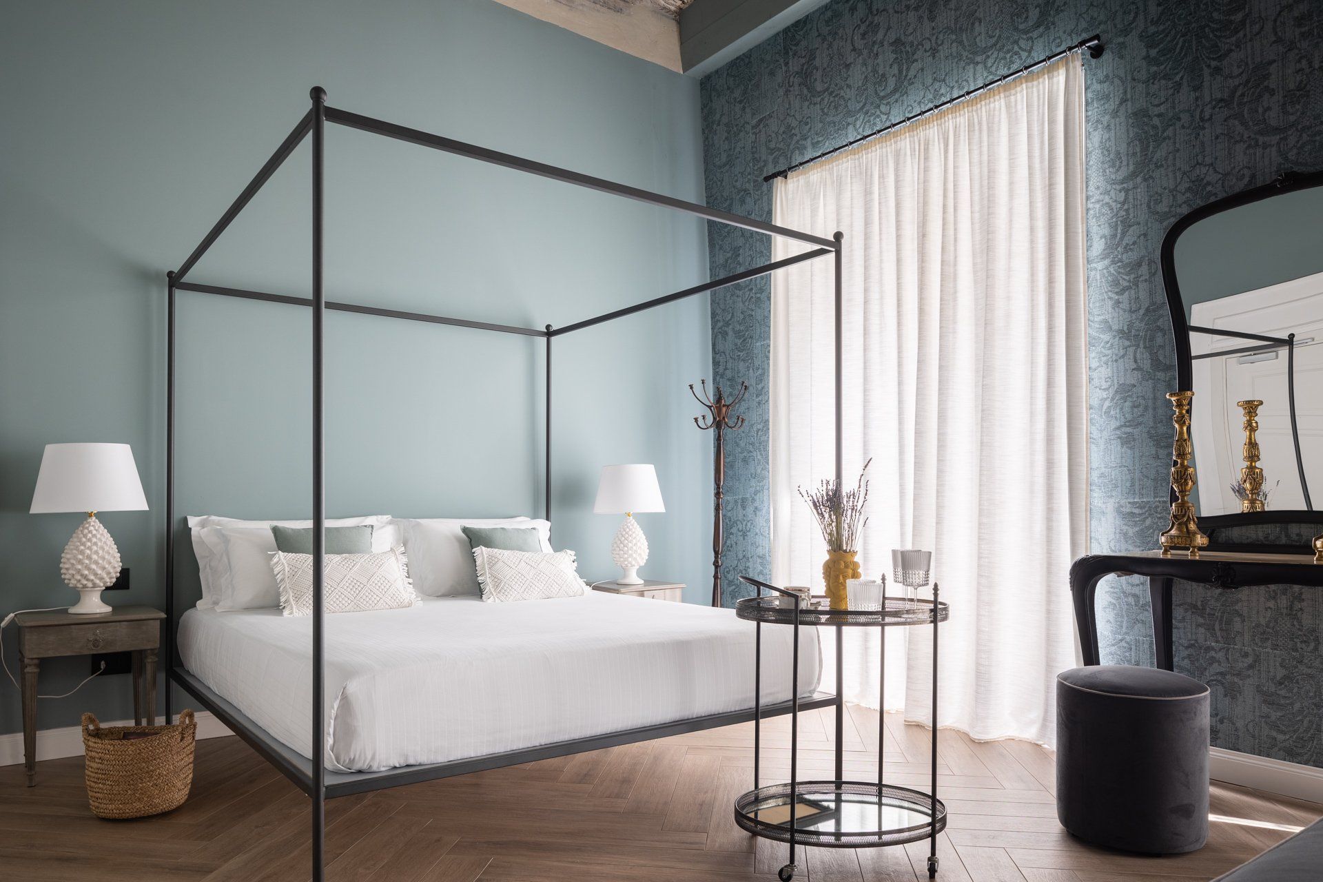 Chambre avec lit à baldaquin, murs bleus, parquet et coiffeuse avec miroir.