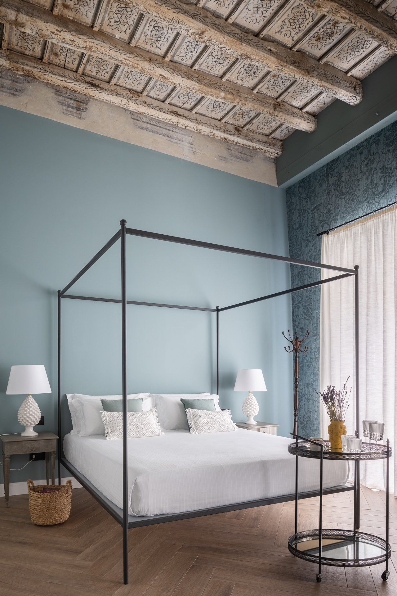 Camera da letto con letto a baldacchino, pareti blu, soffitto decorato e tavolino con lampade.