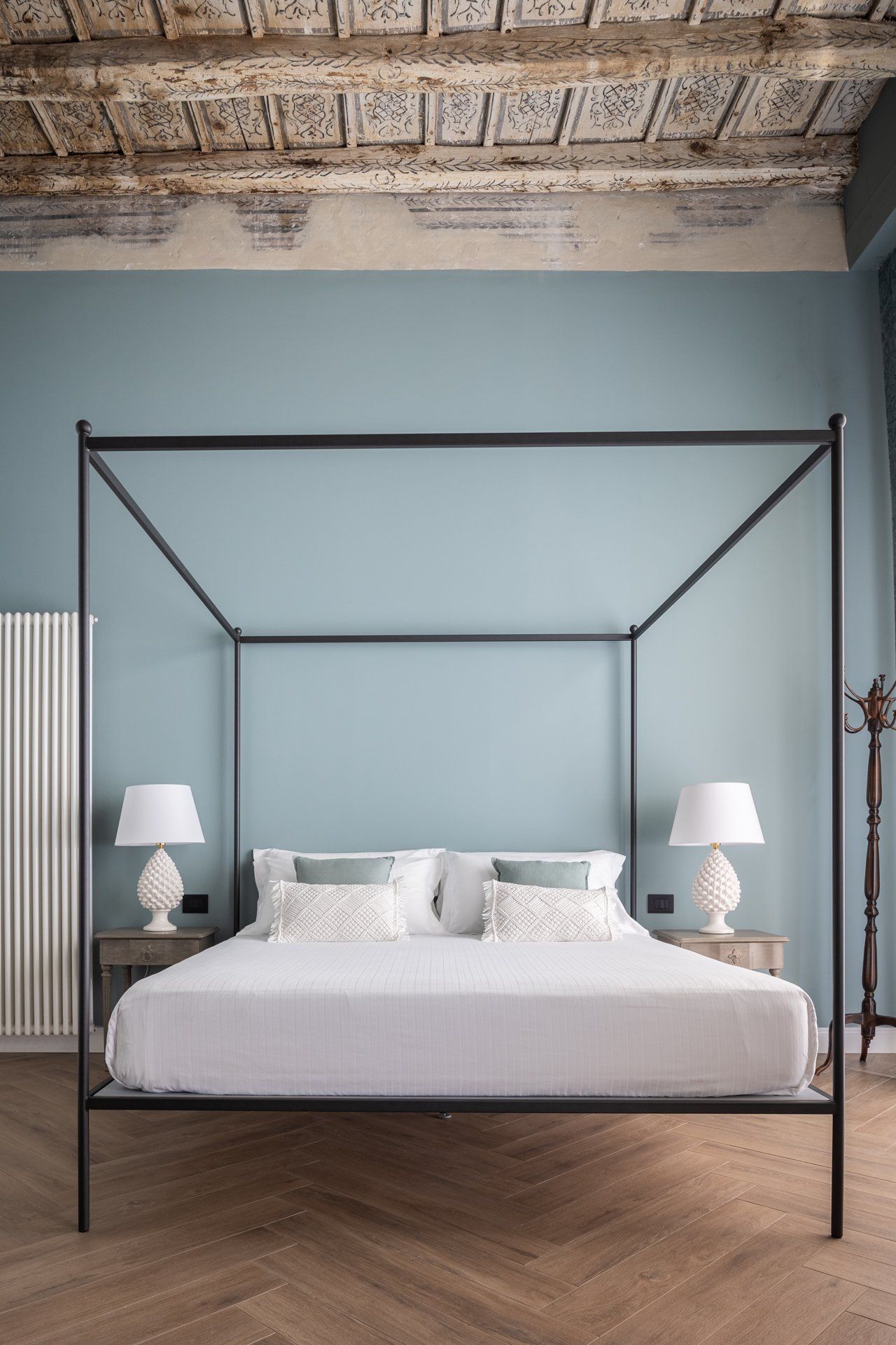 Camera da letto con letto a baldacchino, parete azzurra, pavimento in legno, due lampade da comodino e soffitto decorativo.