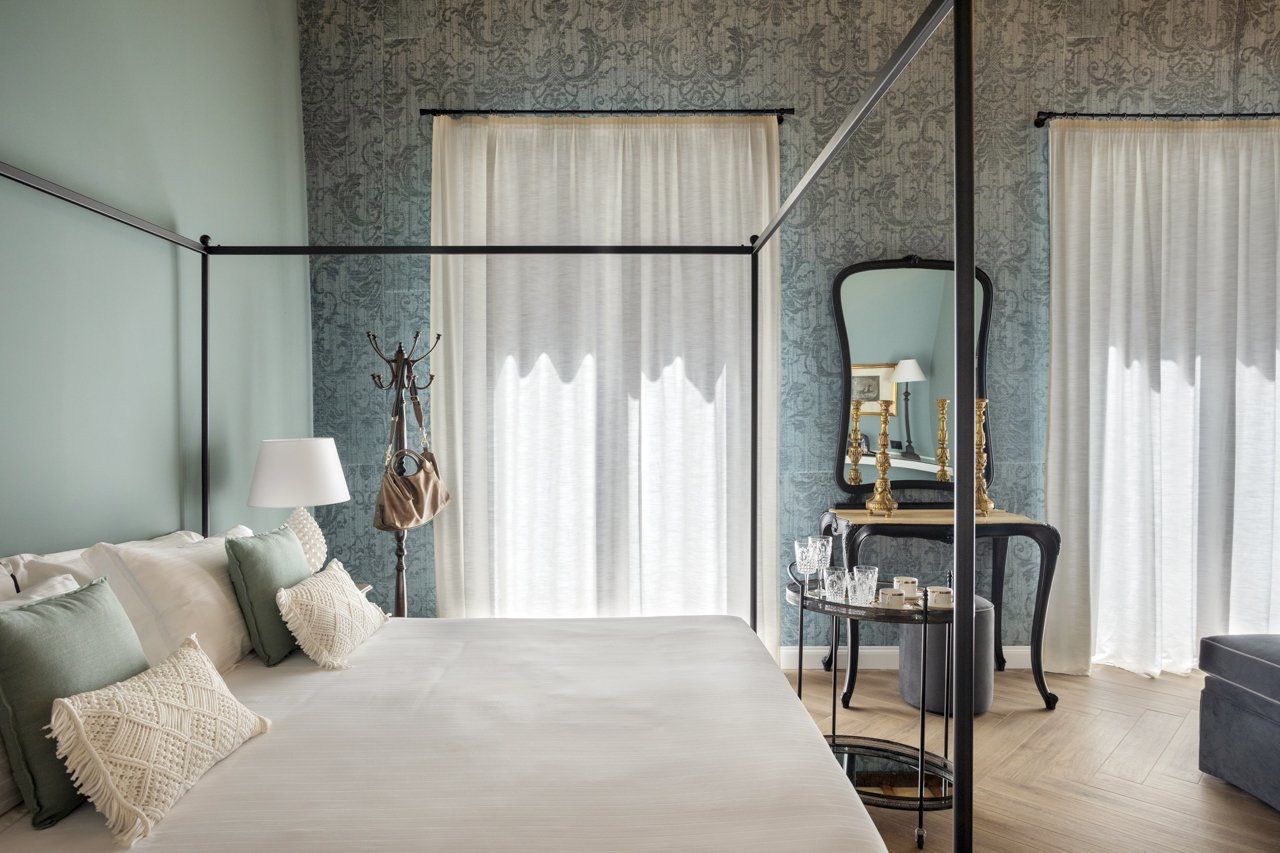 Chambre avec lit à baldaquin, murs vert clair, papier peint à motifs et voilages.