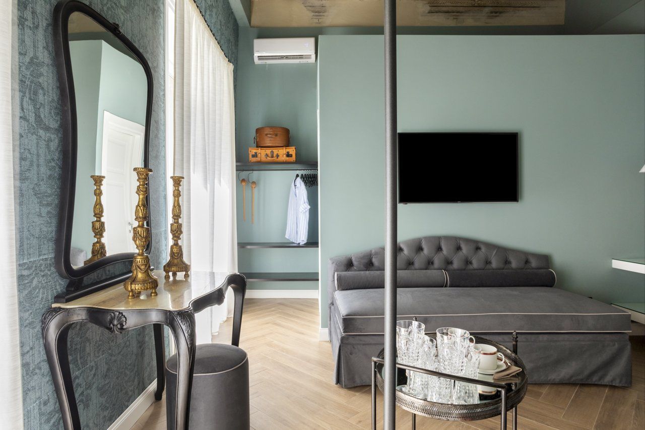 Elegante camera d'albergo con pareti color verde acqua, mobiletto per il trucco, divano letto e TV.