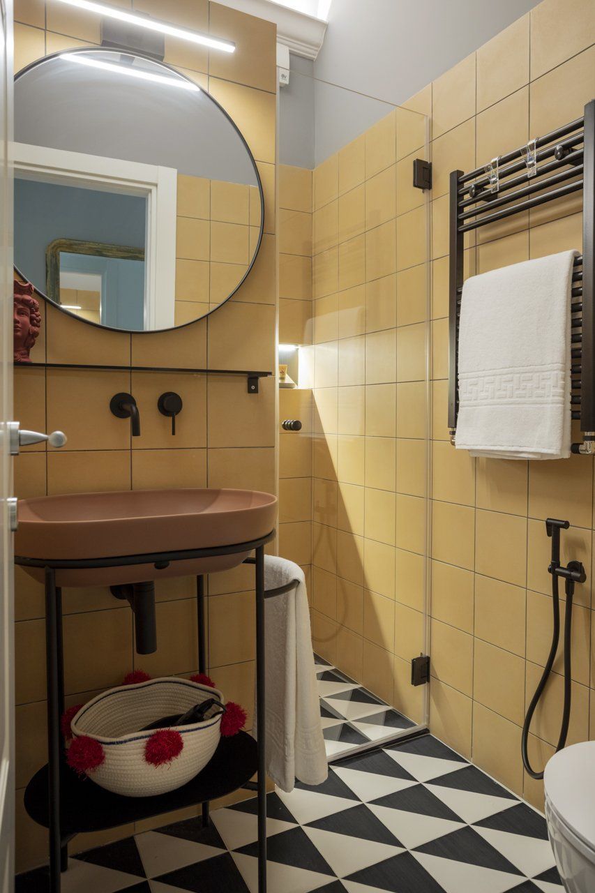 Bagno piastrellato di giallo con pavimento bianco e nero. Dispone di uno specchio rotondo.