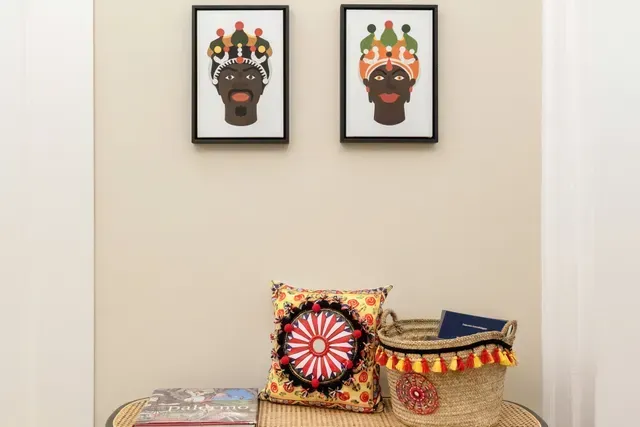 Deux portraits encadrés au-dessus d'un banc avec un coussin, un panier et des livres. Fond mural neutre.