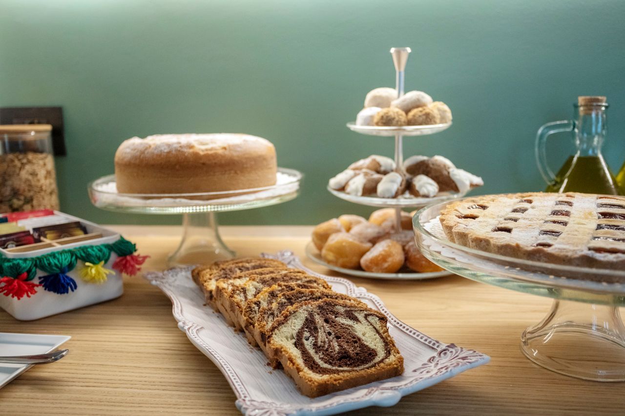 Assortimento di dolci su un tavolo di legno, tra cui una torta e una crostata, con una bottiglia di olio sullo sfondo.