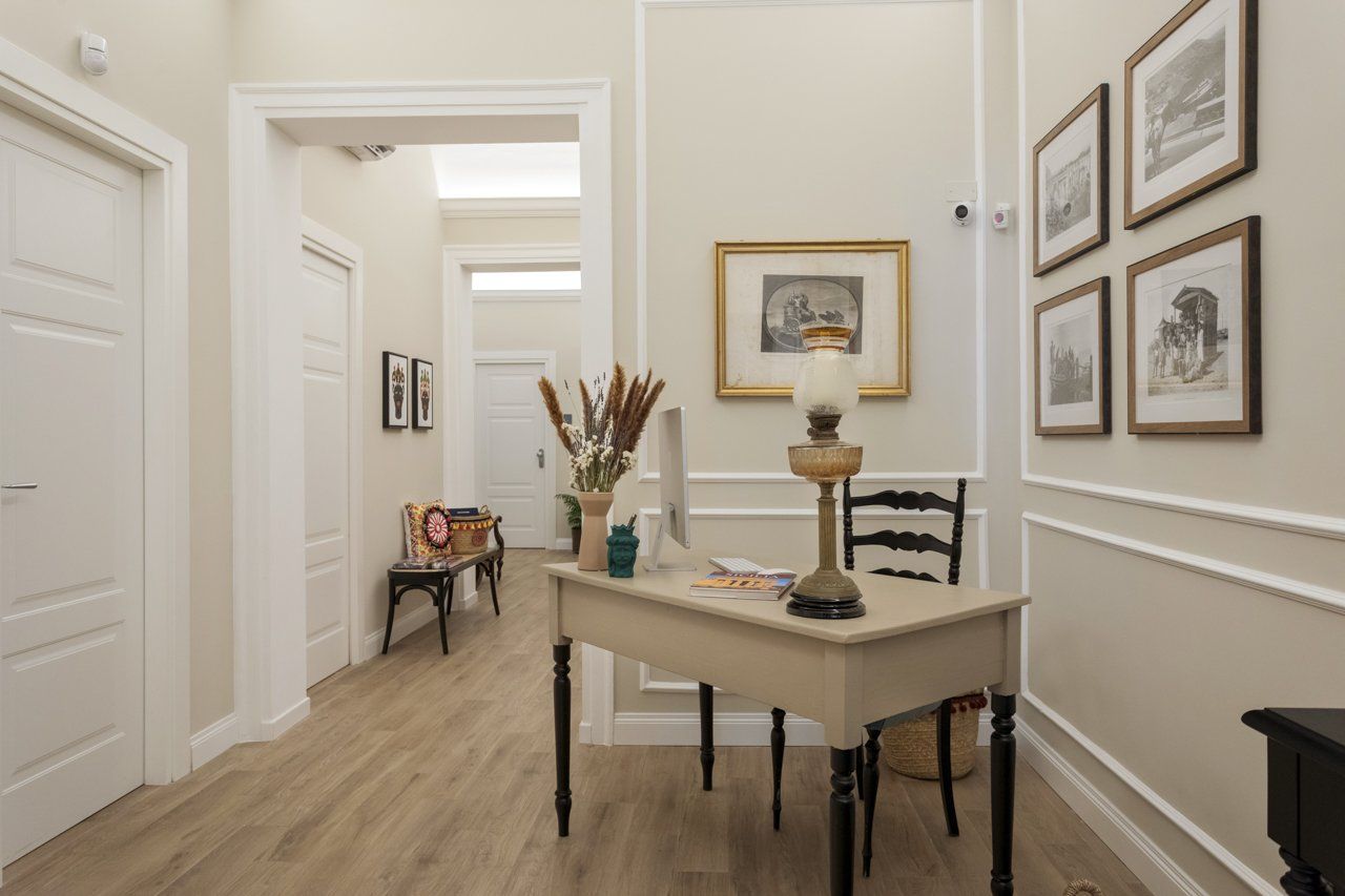 Couloir avec bureau, œuvres d'art et moulures blanches. Le parquet clair et les murs aux tons neutres créent un espace lumineux.