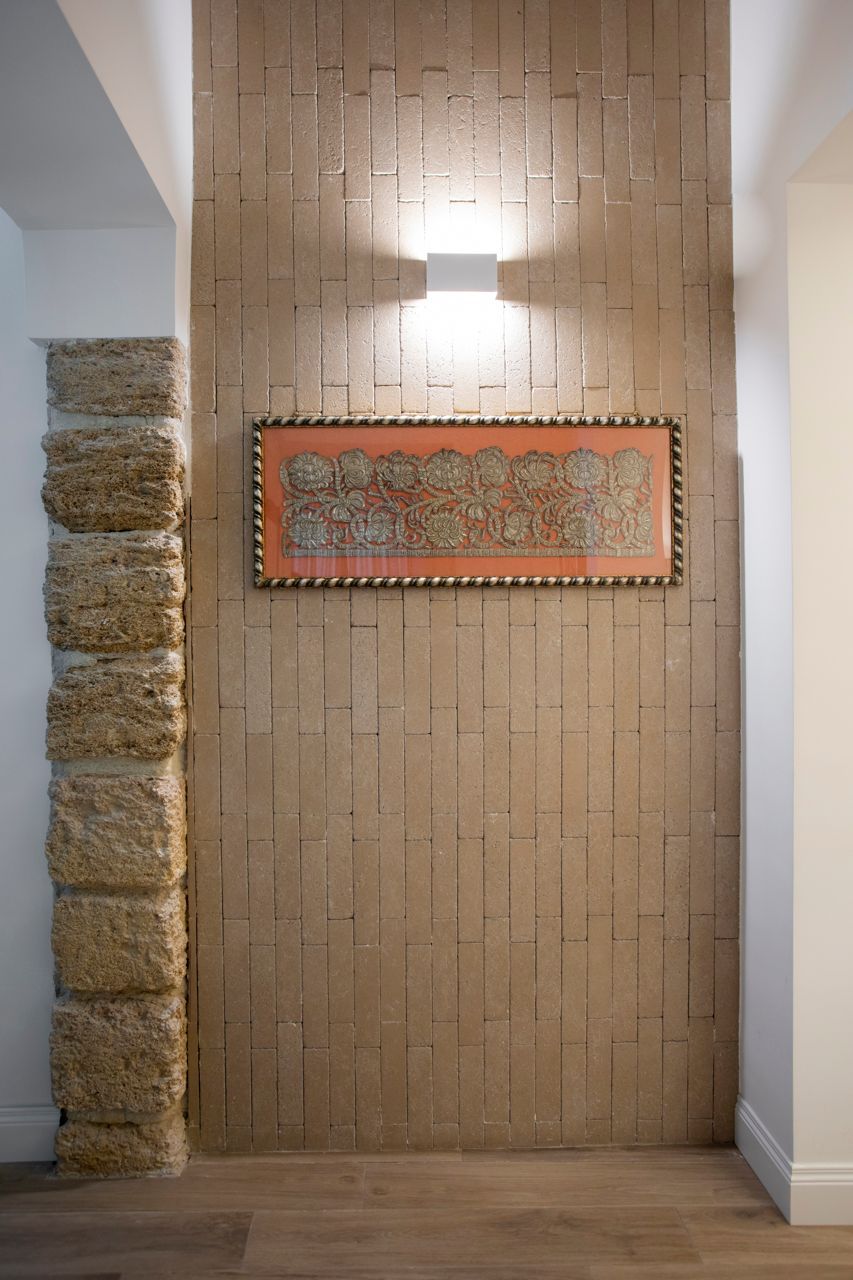 Parete con pietra lavorata e opere d'arte, illuminata da un'applique. Colonna in pietra sulla sinistra.