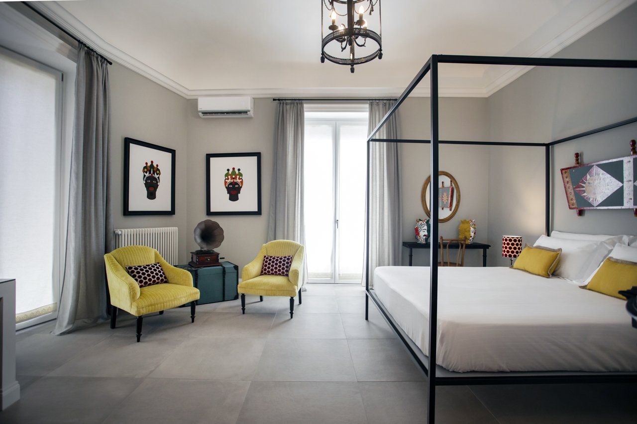 Chambre avec fauteuils jaunes, cadre de lit noir, murs gris et œuvres d'art encadrées.