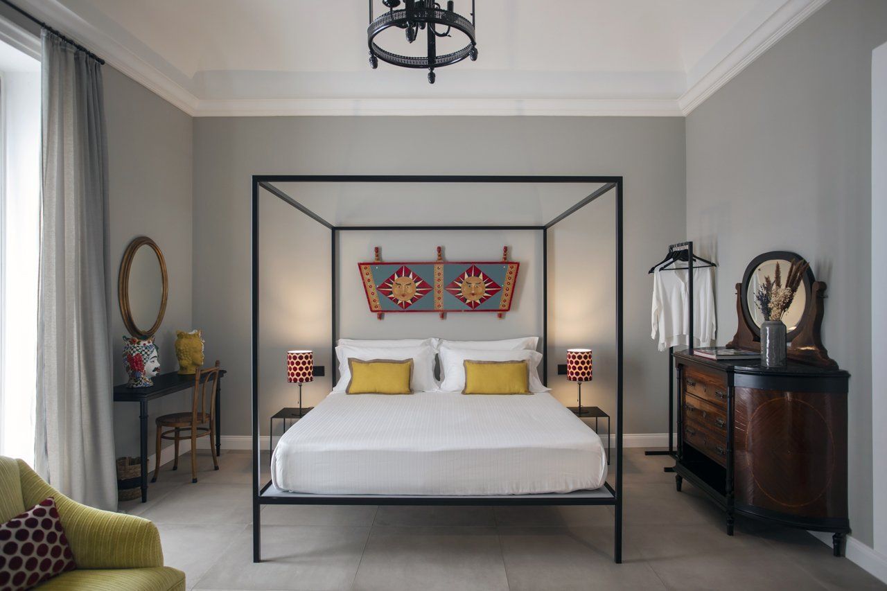 Chambre avec lit à baldaquin, murs gris, meubles anciens et touches de jaune.