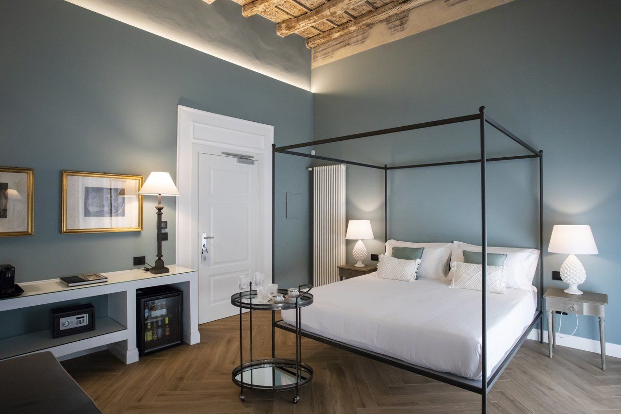 Elegante camera d'albergo con letto a baldacchino, pareti color verde acqua, pavimento in legno e lampade decorative.