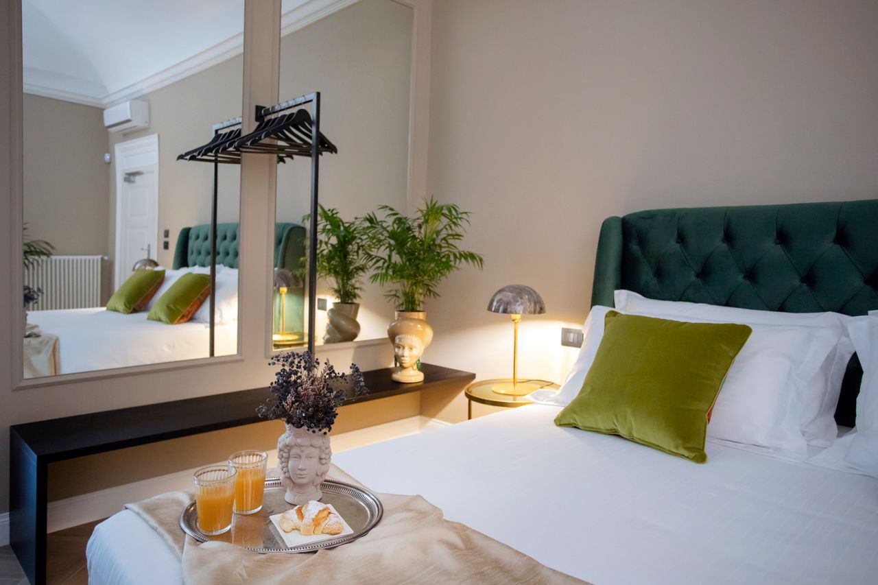 Bedroom with a green tufted headboard, mirror, and a tray with drinks.