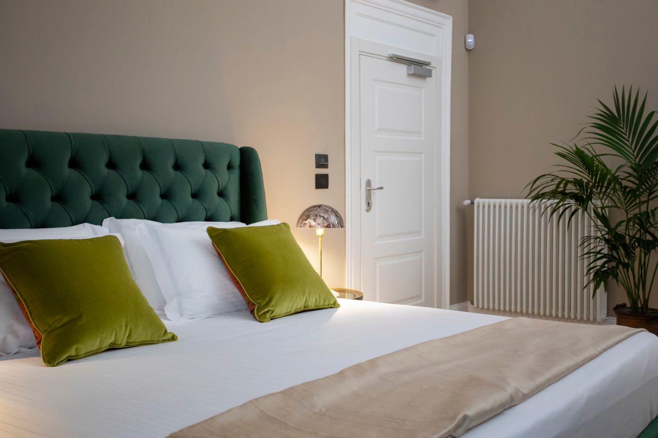 Bedroom with a green tufted headboard, white bedding, and green pillows. A potted plant stands next to a white door.