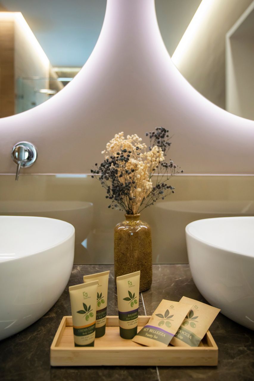Bathroom with two sinks, toiletries on a tray, and a vase with dried flowers.