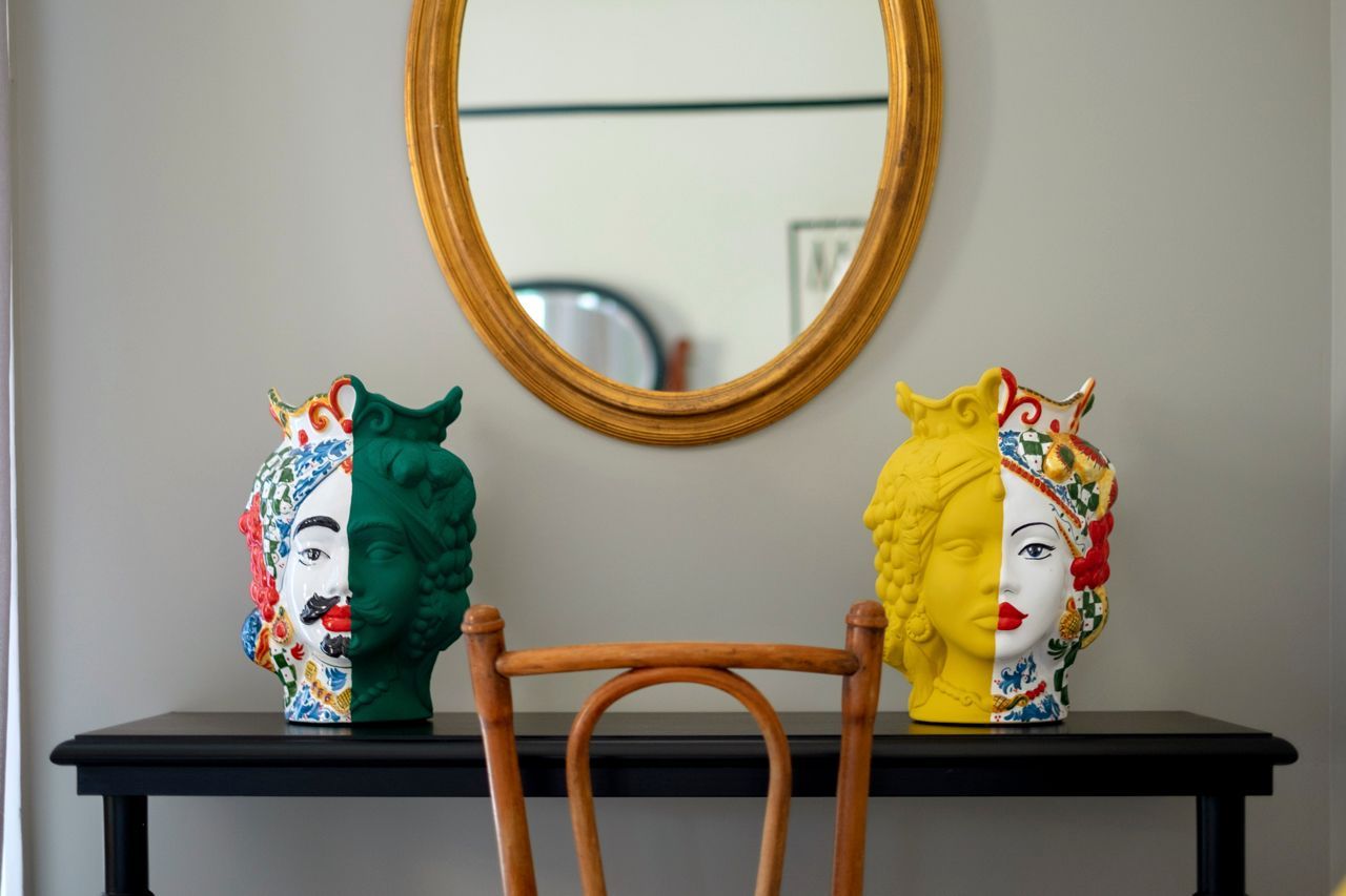 Due vasi colorati in ceramica a forma di testa, uno specchio dorato sopra un tavolo nero.