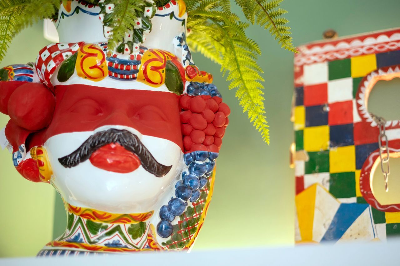 Vaso in ceramica colorata con baffi e felce, accanto a decorazioni a scacchi.