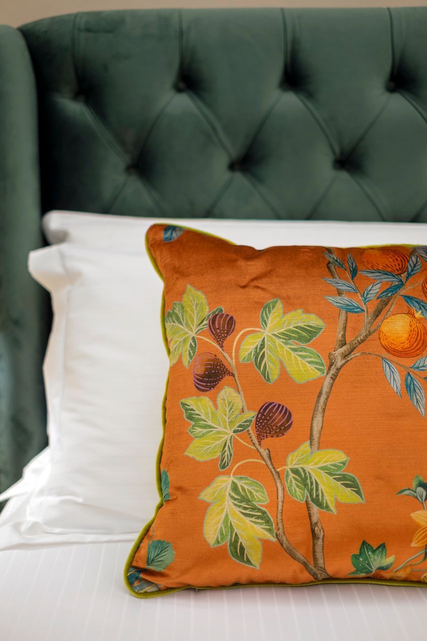 Orange floral pillow on white sheets, with a green tufted headboard in the background.