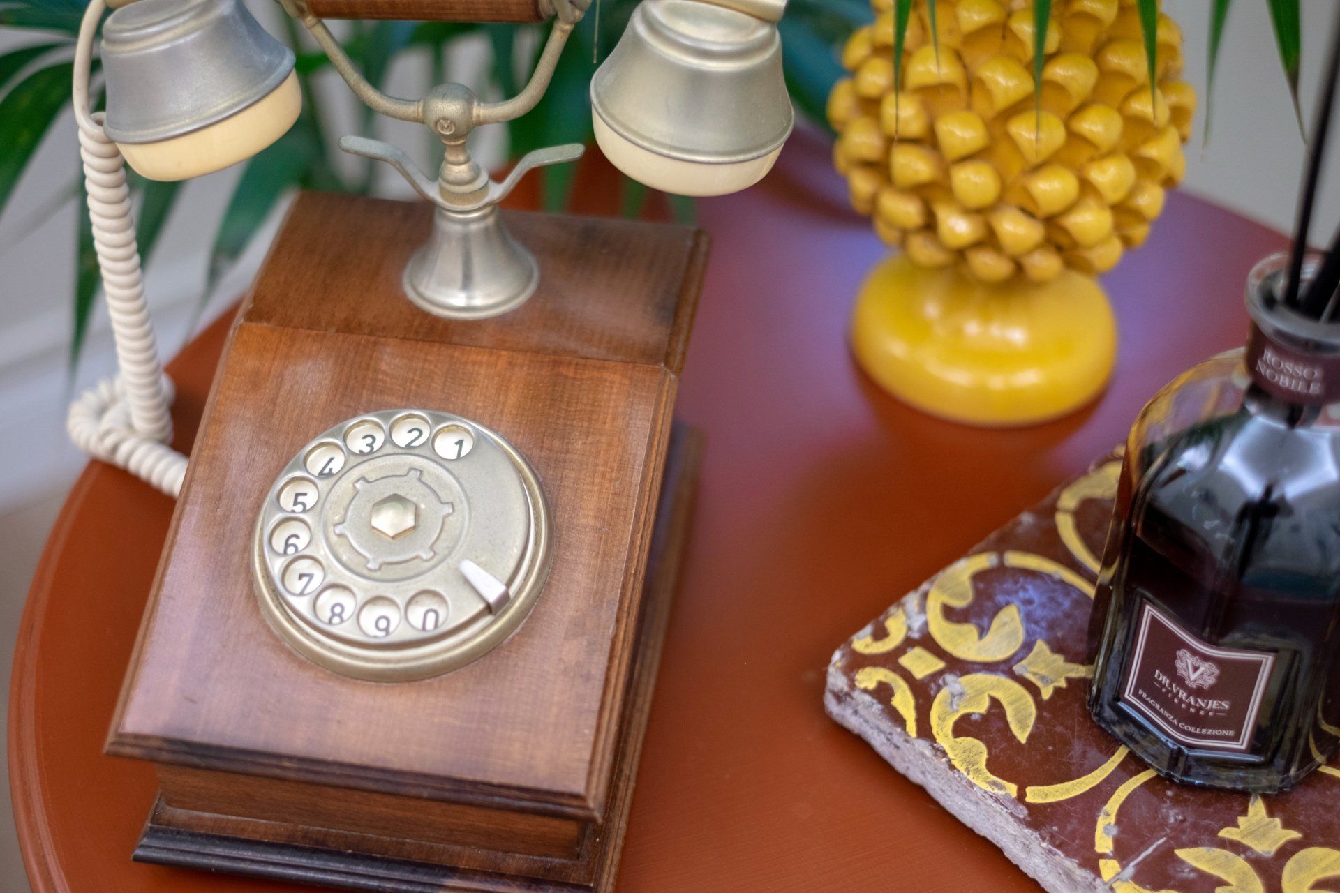 Telefono a disco d'epoca su un tavolo marrone con decorazione a forma di ananas e diffusore a bastoncini.