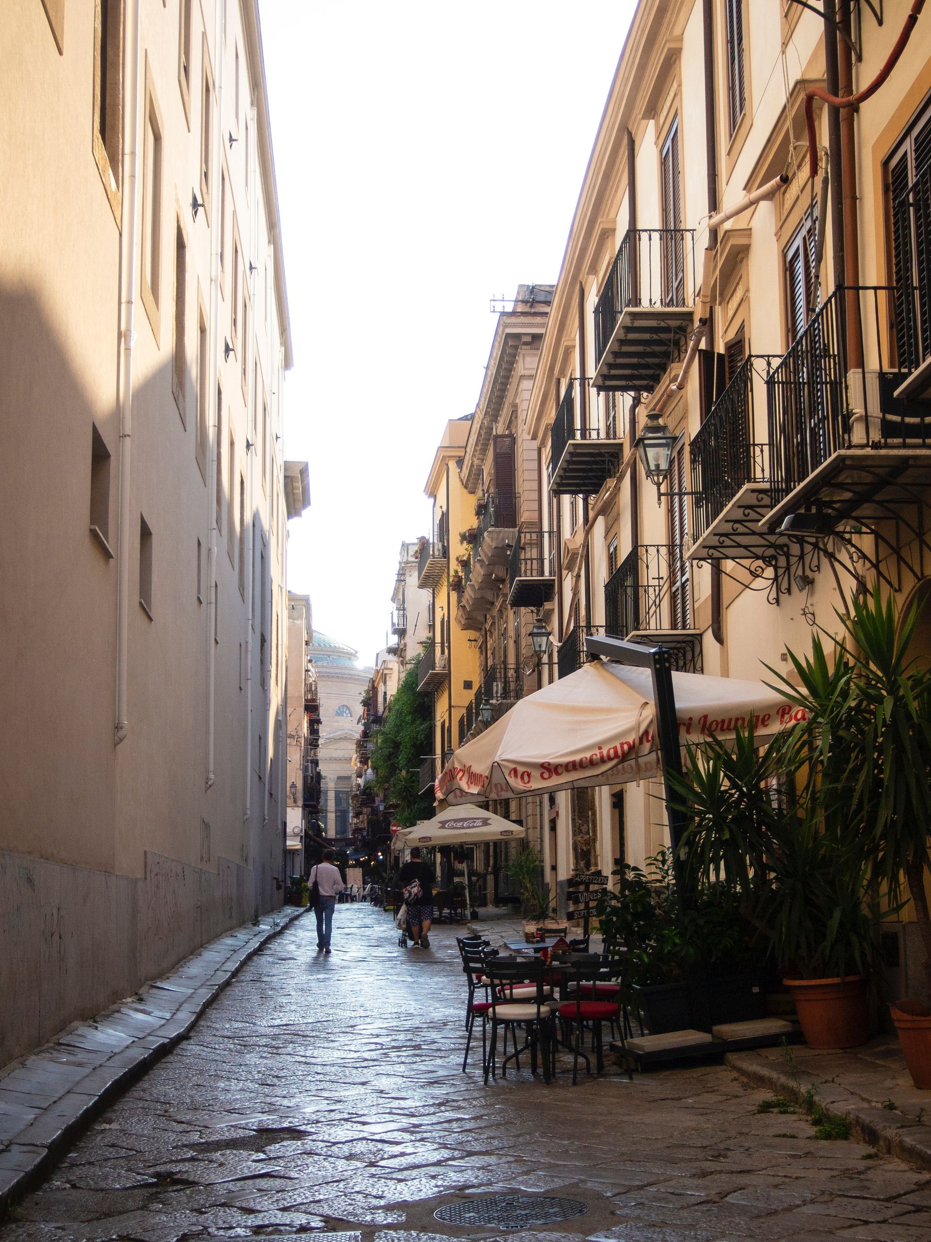 Rue pavée à Palerme, en Italie, bordée de bâtiments et de terrasses de cafés.