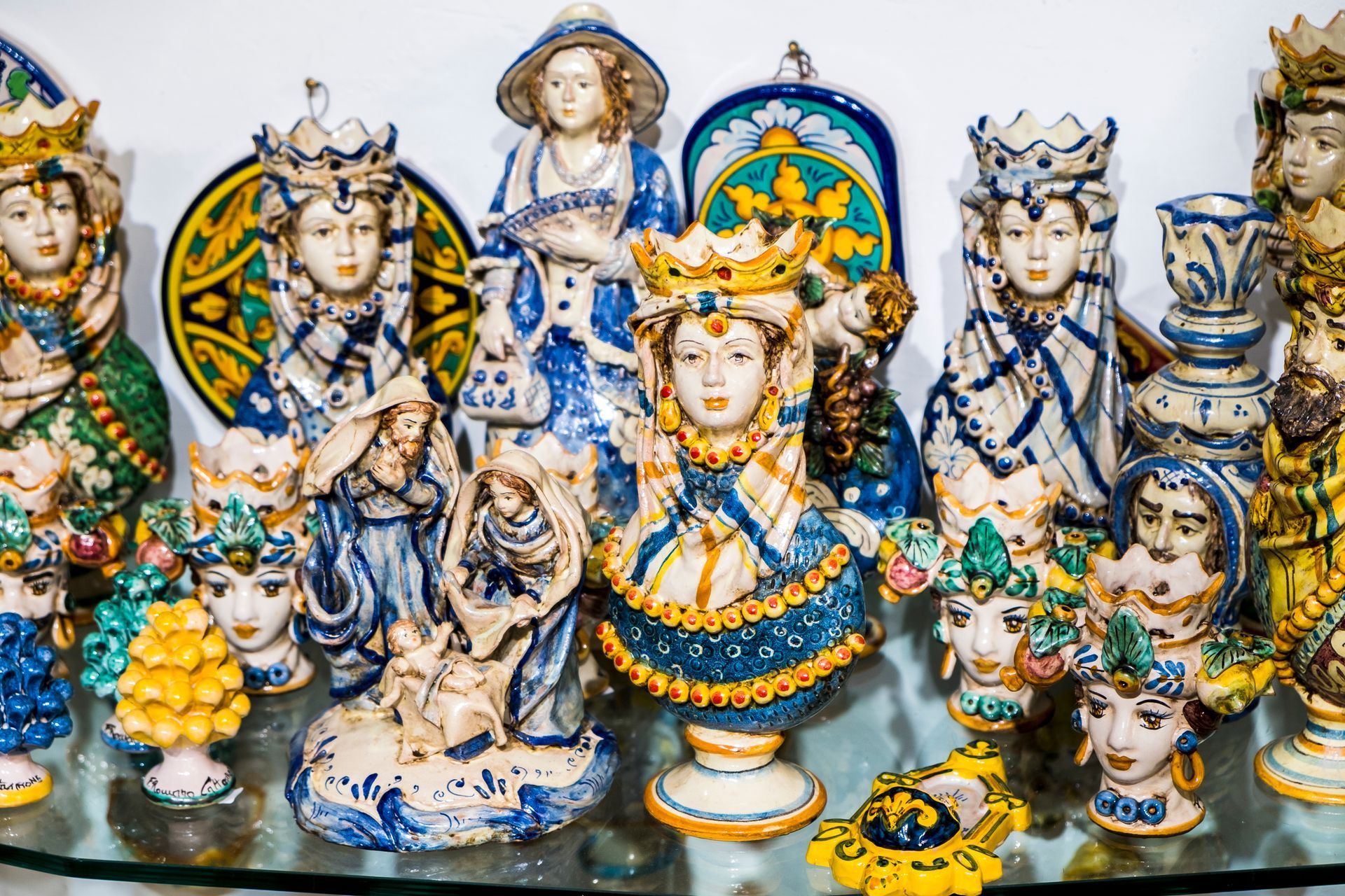 Collection de bustes en céramique colorés et d'objets décoratifs, principalement bleus et blancs, sur une étagère en verre.