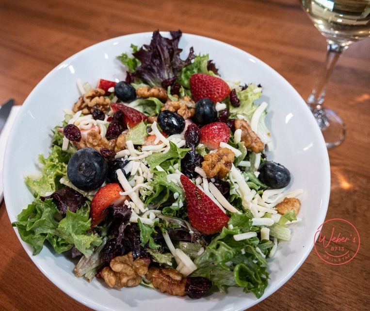 A salad with strawberries , blueberries , walnuts , cheese and a glass of wine on a table.