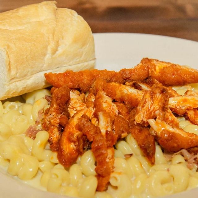 A plate of macaroni and cheese with chicken and a loaf of bread.