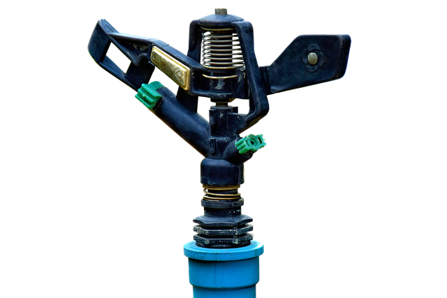 Blue sprinkler head with black arms and green nozzles on a pipe