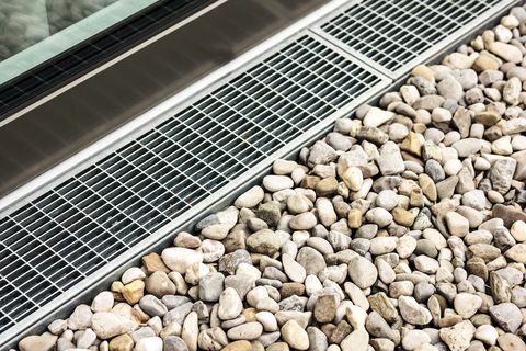 Metal drainage grate beside a bed of rounded gray and beige stones