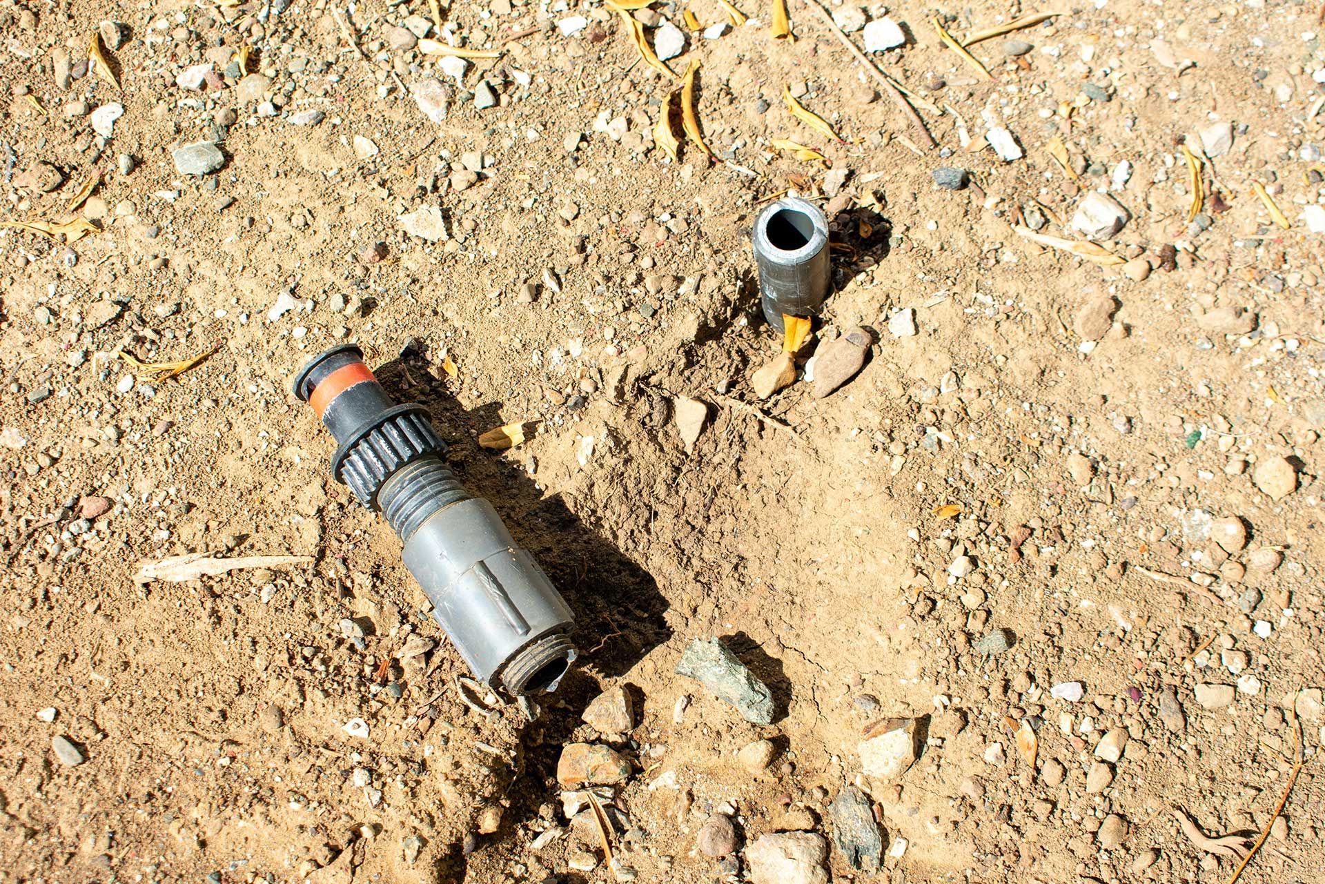 A metal grenade and a loose cap lying on sandy ground among small rocks.
