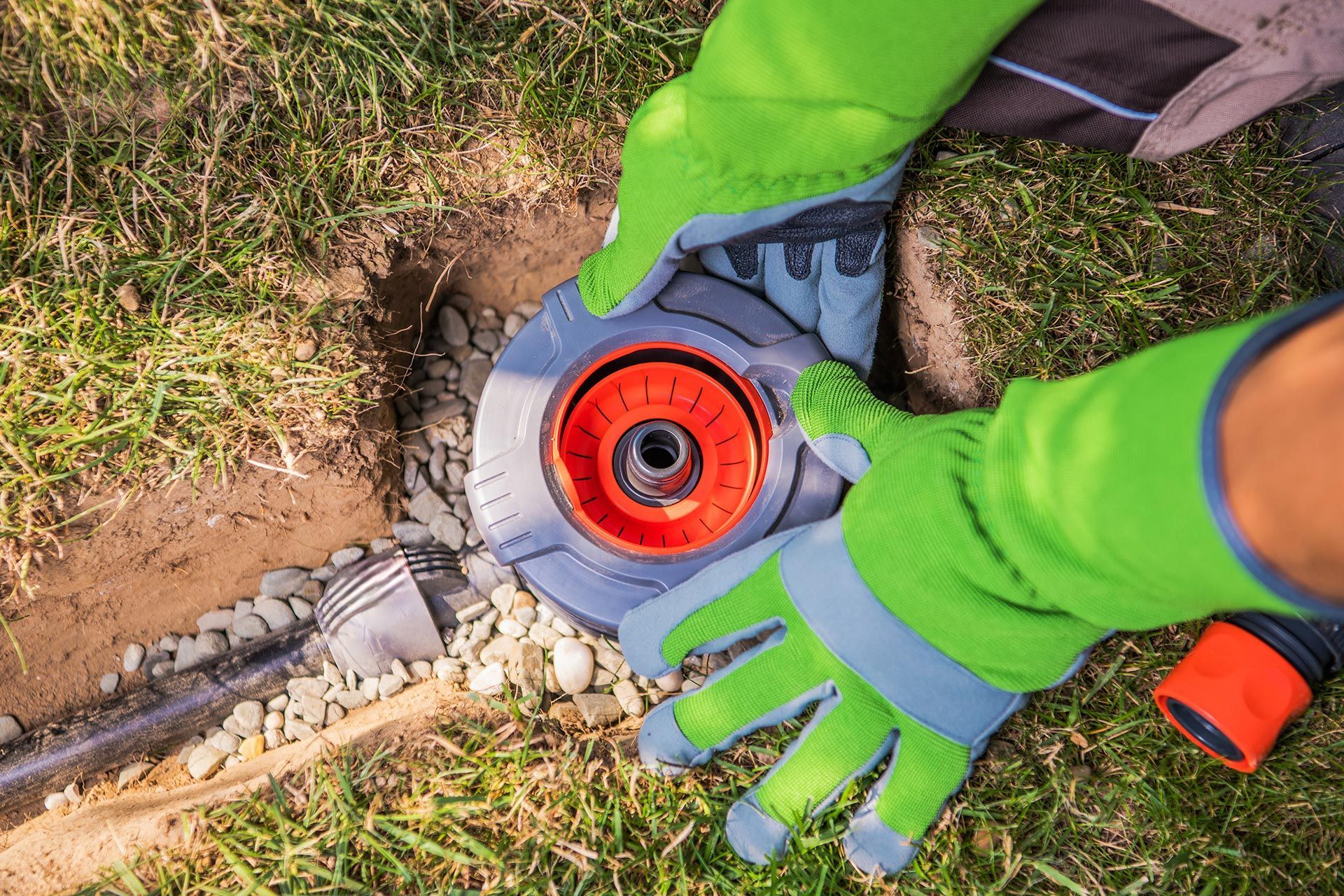 Gloved hands using a circular saw on stone pavers beside grass and soil