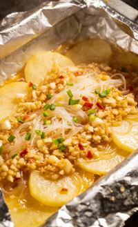 Foil packet with sliced potatoes topped with minced garlic, green onions, and sauce