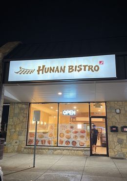 Hunan Bistro storefront at night with lit sign, glass entrance, and menu photos in the window