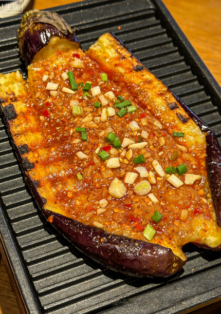 Grilled eggplant topped with minced garlic and sauce on a black ridged plate