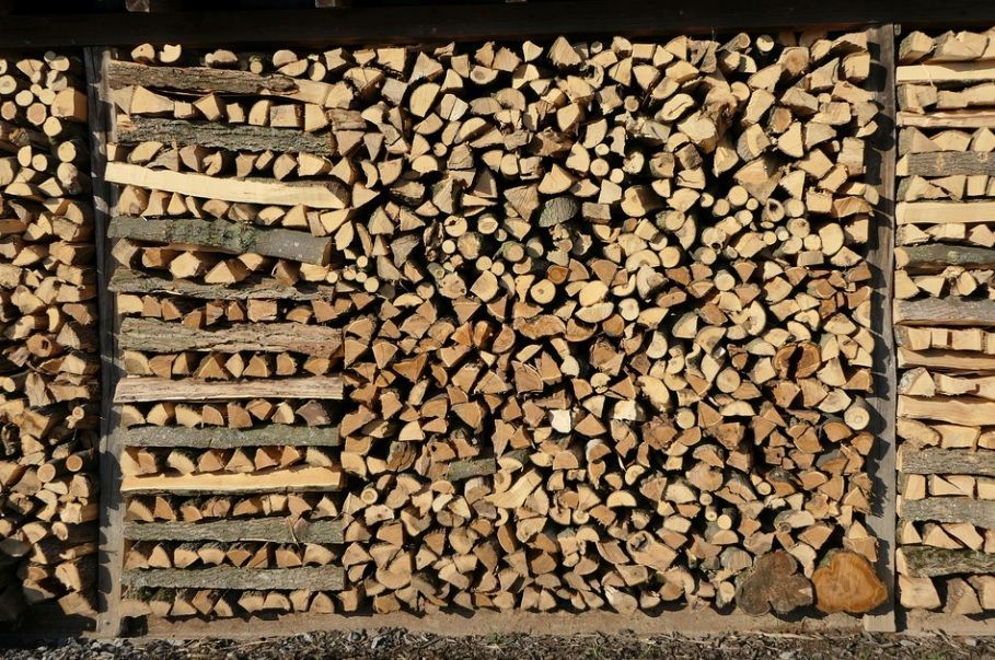Stacked firewood logs in a neatly arranged woodpile with a mix of cut ends and bark visible.