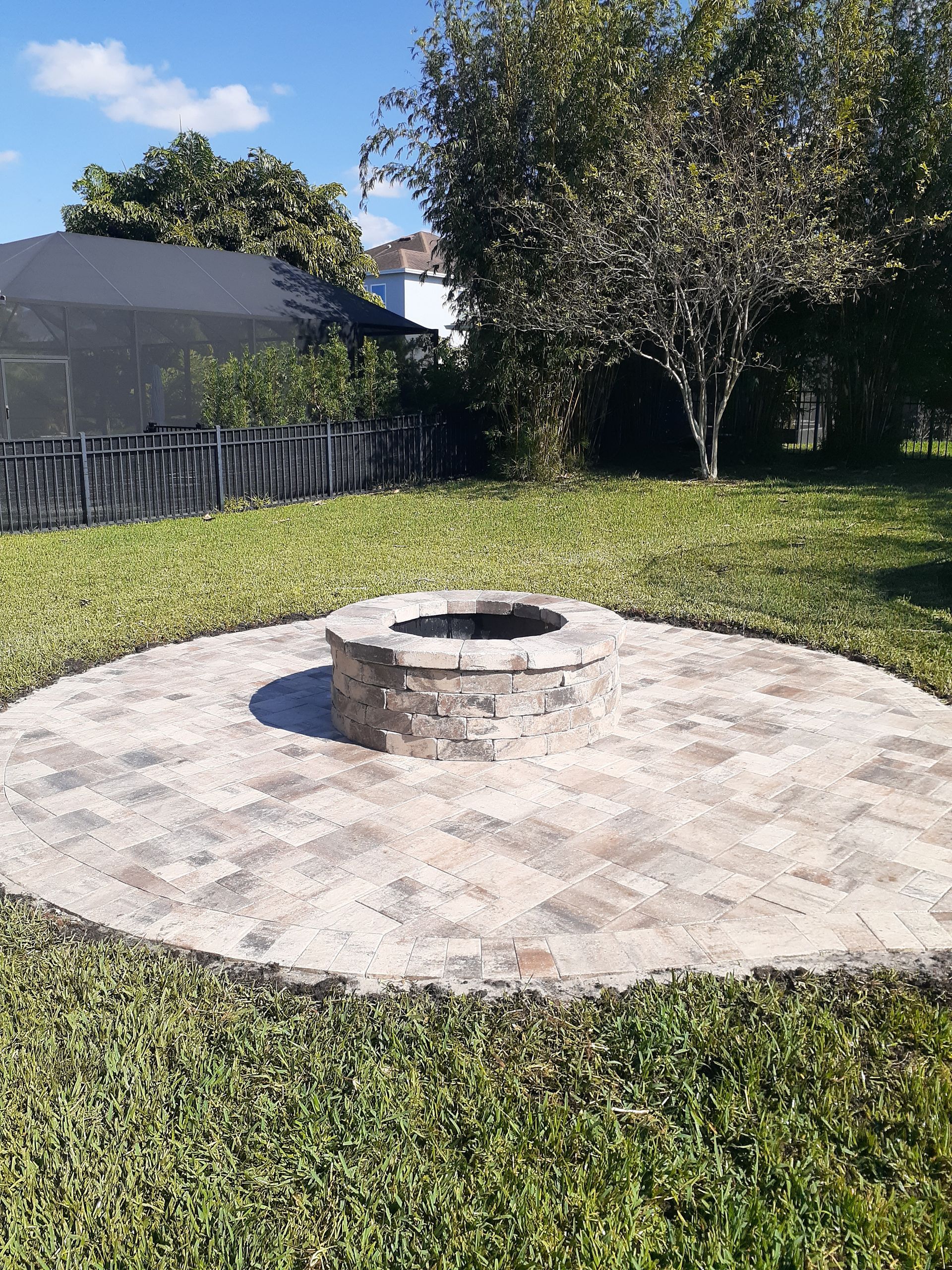 Backyard fire pit on a circular stone patio surrounded by grass and trees.