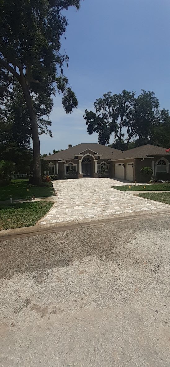 Gravel driveway leading to a single-story house with arches and trees on a sunny day